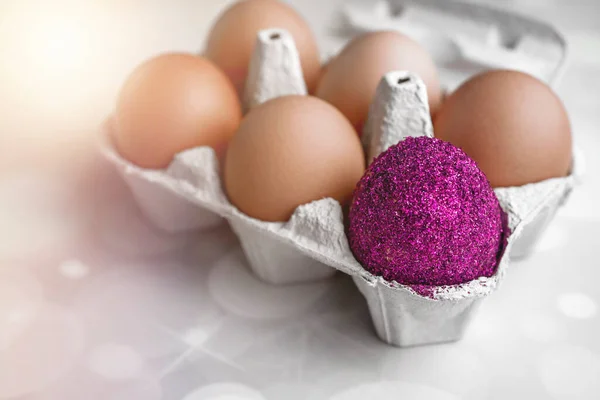 One colored egg among the uncolored on a package container. Trendy Easter glitter colored egg. Easter concept. Not like everyone else concept. Macro close up