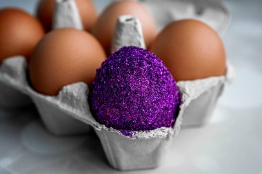 Renksizler arasında bir renkli yumurta bir paket konteynırın üzerinde. Paskalya ışıltısı renkli yumurta. Paskalya konsepti. Herkes gibi değil. Makro, kapat.