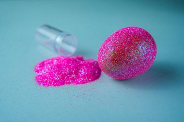 Moda Paskalya arkaplanı, parlak pembe renkli yumurta, mavi ışıklı arka plan ve boş sim tozu şişesi. Paskalya konsepti. Boyalı tavuk yumurtasıyla yaratıcı bir bahar tatili resmi.