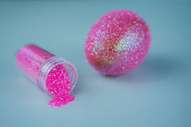 Moda Paskalya arkaplanı, parlak pembe renkli yumurta, mavi ışıklı arka plan ve boş sim tozu şişesi. Paskalya konsepti. Boyalı tavuk yumurtasıyla yaratıcı bir bahar tatili resmi.