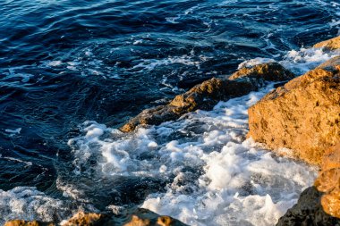 Dalgalar sabahları sahilde kayalara çarpıyor. Dalgalı denizde gün doğumu kayalarla. 