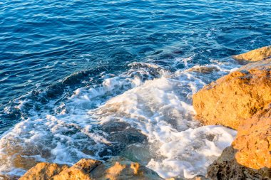 Dalgalar sabahları sahilde kayalara çarpıyor. Dalgalı denizde gün doğumu kayalarla. 