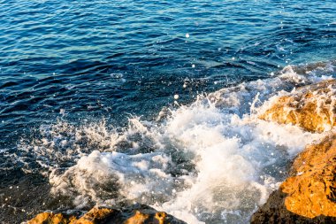 Dalgalar sabahları sahilde kayalara çarpıyor. Dalgalı denizde gün doğumu kayalarla. 