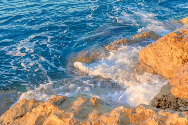 Dalgalar sabahları sahilde kayalara çarpıyor. Dalgalı denizde gün doğumu kayalarla. 