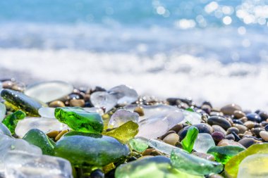 Deniz kıyısındaki doğal cilalı cam ve taşlar. Dalgalı açık deniz suyu. Yakından bakınca çok renkli deniz taşları olan yeşil, parlak camlar. Plaj yaz geçmişi. 