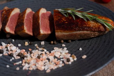Grilled Duck Breast Slices. Served on the dark plate, wooden table background. 