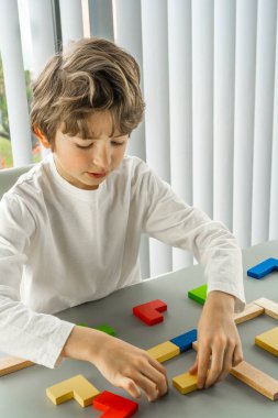 Gri arka planda tahta küple oynayan bir çocuk. Masada çok renkli küpler var. Ahşap arka planda geometrik şekiller. Bulmaca konsepti. Yüksek kalite fotoğraf