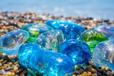 Deniz kıyısındaki güzel cam ve taşlar. Dalgalı açık deniz suyu. Yakından bakınca çok renkli deniz taşları olan yeşil, parlak camlar. Plaj yaz geçmişi. Yüksek kalite fotoğraf