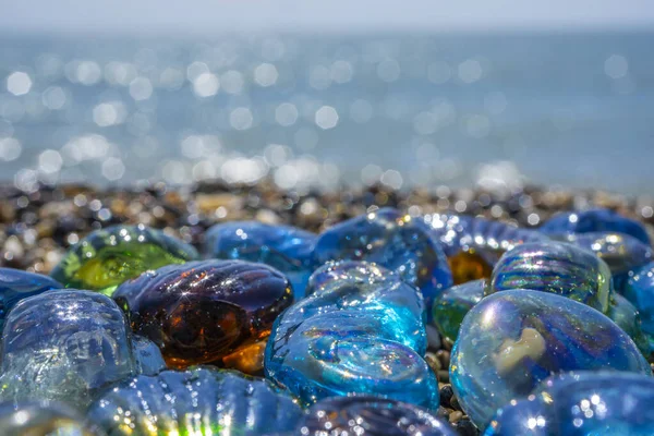 Όμορφο σχήμα γυαλί και πέτρες στην παραλία. Γαλάζιο καθαρό θαλασσινό νερό με κύματα. Πράσινο, μπλε γυαλιστερό γυαλί με πολύχρωμα βότσαλα της θάλασσας από κοντά. Καλοκαιρινό φόντο — Φωτογραφία Αρχείου