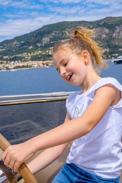 En liten flicka som sitter vid ratten på en yacht. Sjöresa på båten. Sommarresa och semester. barndom och lycka koncept. — Stockfoto