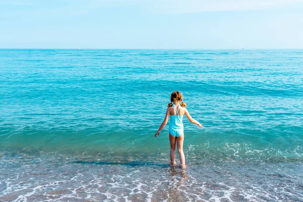 Giovane ragazza che va a fare una nuotata sull'acqua di mare in spiaggia. Goditi la calda acqua di mare nella calda giornata estiva. Vista posteriore sulla ragazza che cammina sulla sabbia. Copia spazio — Foto Stock