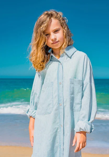Молодая красивая девушка в синем платье, остановившаяся на песчаном пляже возле волн. — стоковое фото