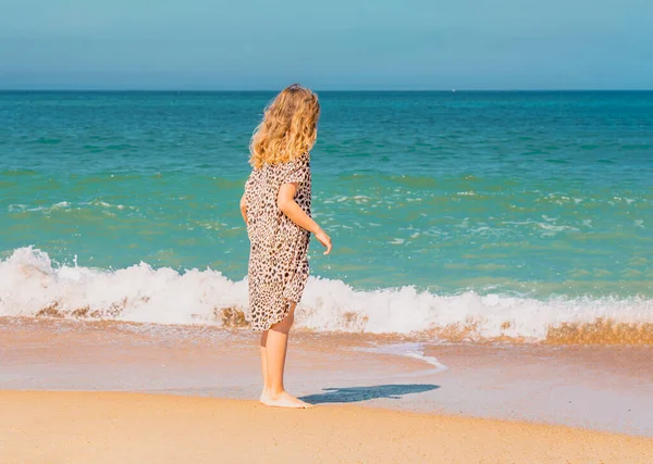 Junge schöne Mädchen in beigem Kleid bleiben am Sandstrand in der Nähe der Wellen. — Stockfoto