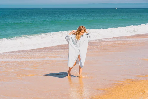 Jeune belle fille en robe bleue courant sur la plage de sable près des vagues. — Photo