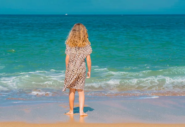 Joven chica hermosa en vestido beige corriendo en la playa de arena cerca de las olas. — Foto de Stock