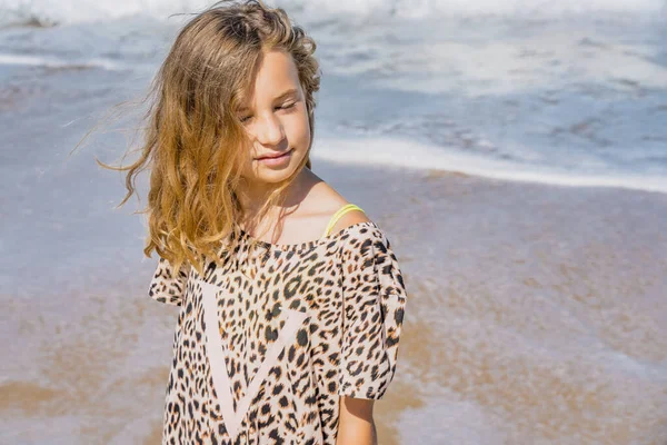 Giovane bella ragazza in abito beige stare lungo la spiaggia di sabbia vicino alle onde. — Foto Stock
