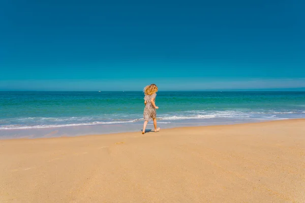 Joven chica hermosa en vestido beige corriendo en la playa de arena cerca de las olas. — Foto de Stock