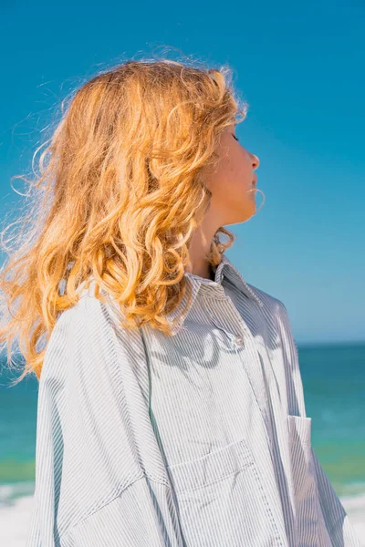 Νεαρό όμορφο κορίτσι σε μπλε φόρεμα που διαμένουν κατά μήκος της αμμώδους παραλίας κοντά στα κύματα. — Φωτογραφία Αρχείου