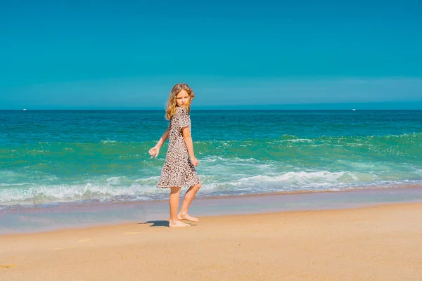 Joven chica hermosa en vestido beige corriendo en la playa de arena cerca de las olas. — Foto de Stock