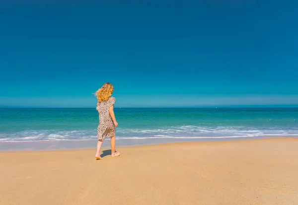Junges schönes Mädchen in beigem Kleid läuft am Sandstrand in der Nähe der Wellen. — Stockfoto