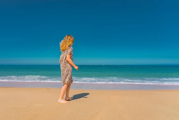 Joven chica hermosa en vestido beige corriendo en la playa de arena cerca de las olas. — Foto de Stock