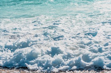 Kum kıyısı ve güzel bir su sıçratma dalgası. Temiz kumlu bir kıyıda köpüklü beyaz dalga, seçici bir odak. Fotokopi alanı olan organik doğal yaz fotoğrafı. Arkadaki mavi yumuşak dalga.