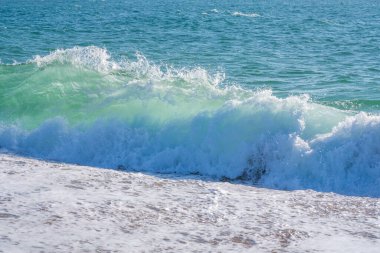  Kum kıyısı ve güzel bir su sıçratma dalgası. Temiz kumlu bir kıyıda köpüklü beyaz dalga, seçici bir odak. Fotokopi alanı olan organik doğal yaz fotoğrafı. Arkadaki mavi yumuşak dalga.