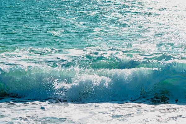 Sandy coast with a beautiful splash wave. Foaming white wave on a clean sandy shore, selective focus. Organic natural summer photo with copy space. Blue soft wave as background. — Stock Photo, Image