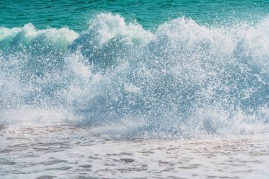 Kum kıyısı ve güzel bir su sıçratma dalgası. Temiz kumlu bir kıyıda köpüklü beyaz dalga, seçici bir odak. Fotokopi alanı olan organik doğal yaz fotoğrafı. Arkadaki mavi yumuşak dalga.