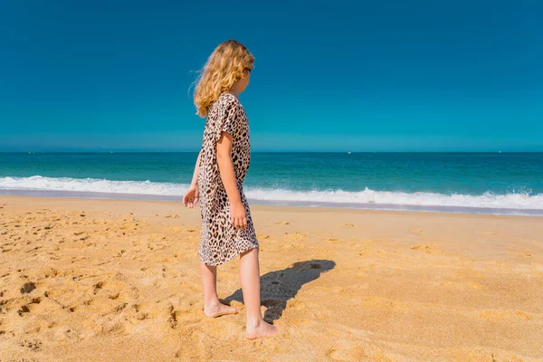 Junges schönes Mädchen in beigem Kleid läuft am Sandstrand in der Nähe der Wellen. — Stockfoto