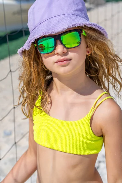 Retrato de uma jovem menina modelo bonita com chapéu e óculos de sol posando na praia. Vestindo um biquíni amarelo brilhante. Dia de verão, areia branca. — Fotografia de Stock