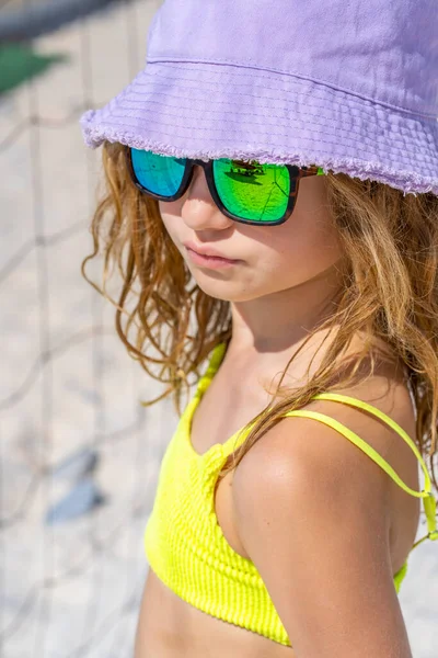 Ritratto di una giovane bella modella con cappello e occhiali da sole in posa sulla spiaggia. Indossa un costume da bagno giallo brillante. Giornata estiva, sabbia bianca. — Foto Stock