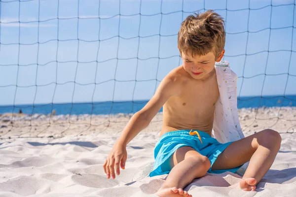 Przystojny chłopak w niebieskich spodenkach i okularach siedzi na białym piasku na plaży. Zabawa z białym piaskiem. — Zdjęcie stockowe