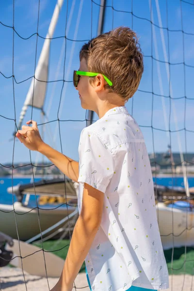 Bel ragazzo in pantaloncini blu e camicia bianca, con gli occhiali da sole in piedi su sabbia bianca su un campo da pallavolo sulla spiaggia. — Foto Stock