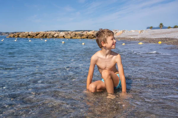 Young boy playing with waves on the beach by the sea. Holidays with children near the sea concept. — Fotografia de Stock