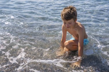 Genç çocuk deniz kenarında dalgalarla oynuyor. Deniz konseptine yakın çocuklarla tatiller..