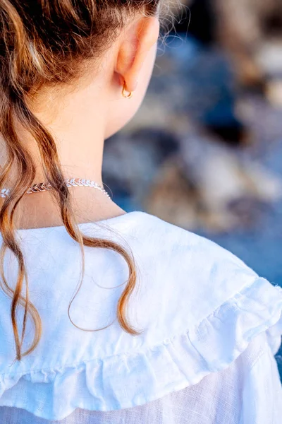 Vista posteriore della ragazza caucasica con lunghi capelli ondulati, indossa un vestito bianco e cammina nell'acqua del mare. Concetto di moda e sessione fotografica di viaggio. — Foto Stock