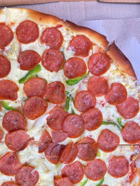 Biberli pizzanın yüksek açılı, yakın plan bir görüntüsü. Sergide erimiş beyaz peynirden bir yatağa dağıtılmış sayısız kırmızı-kahverengi pepperoni bulunuyor..