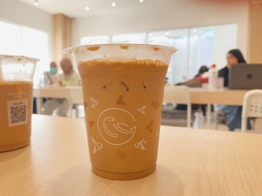 Açık renkli ahşap bir masada otururken soğuk, buzlu bir sütlü kahve ya da temiz bir plastik bardakta latte yakın çekim..