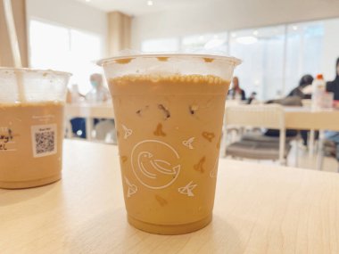 Açık renkli ahşap bir masada otururken soğuk, buzlu bir sütlü kahve ya da temiz bir plastik bardakta latte yakın çekim..