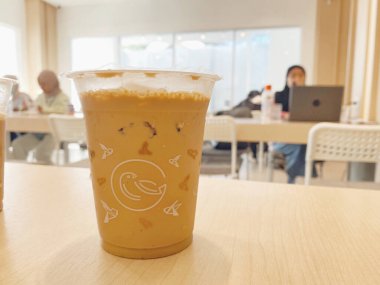 Açık renkli ahşap bir masada otururken soğuk, buzlu bir sütlü kahve ya da temiz bir plastik bardakta latte yakın çekim..