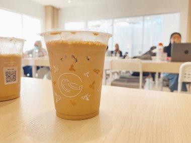 Açık renkli ahşap bir masada otururken soğuk, buzlu bir sütlü kahve ya da temiz bir plastik bardakta latte yakın çekim..