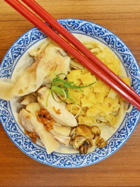 Resim, sıcak, yatay tahıllı ahşap bir masa üzerine kurulmuş mavi ve beyaz bir seramik kasede servis edilen erişte kâsesini yukarıdan aşağıya doğru gösteriyor..