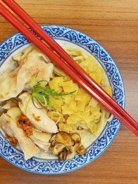 Resim, sıcak, yatay tahıllı ahşap bir masa üzerine kurulmuş mavi ve beyaz bir seramik kasede servis edilen erişte kâsesini yukarıdan aşağıya doğru gösteriyor..