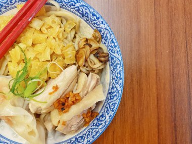 Resim, sıcak, yatay tahıllı ahşap bir masa üzerine kurulmuş mavi ve beyaz bir seramik kasede servis edilen erişte kâsesini yukarıdan aşağıya doğru gösteriyor..