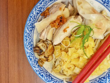 Resim, sıcak, yatay tahıllı ahşap bir masa üzerine kurulmuş mavi ve beyaz bir seramik kasede servis edilen erişte kâsesini yukarıdan aşağıya doğru gösteriyor..