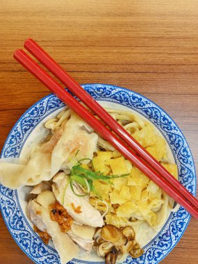 Resim, sıcak, yatay tahıllı ahşap bir masa üzerine kurulmuş mavi ve beyaz bir seramik kasede servis edilen erişte kâsesini yukarıdan aşağıya doğru gösteriyor..