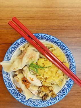 Resim, sıcak, yatay tahıllı ahşap bir masa üzerine kurulmuş mavi ve beyaz bir seramik kasede servis edilen erişte kâsesini yukarıdan aşağıya doğru gösteriyor..