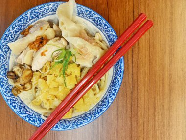 Resim, sıcak, yatay tahıllı ahşap bir masa üzerine kurulmuş mavi ve beyaz bir seramik kasede servis edilen erişte kâsesini yukarıdan aşağıya doğru gösteriyor..