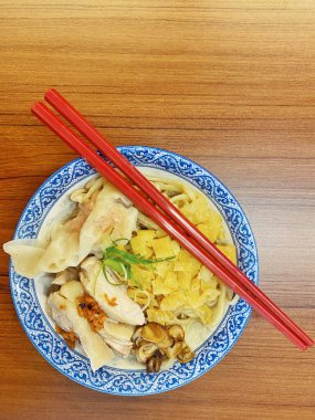 Resim, sıcak, yatay tahıllı ahşap bir masa üzerine kurulmuş mavi ve beyaz bir seramik kasede servis edilen erişte kâsesini yukarıdan aşağıya doğru gösteriyor..